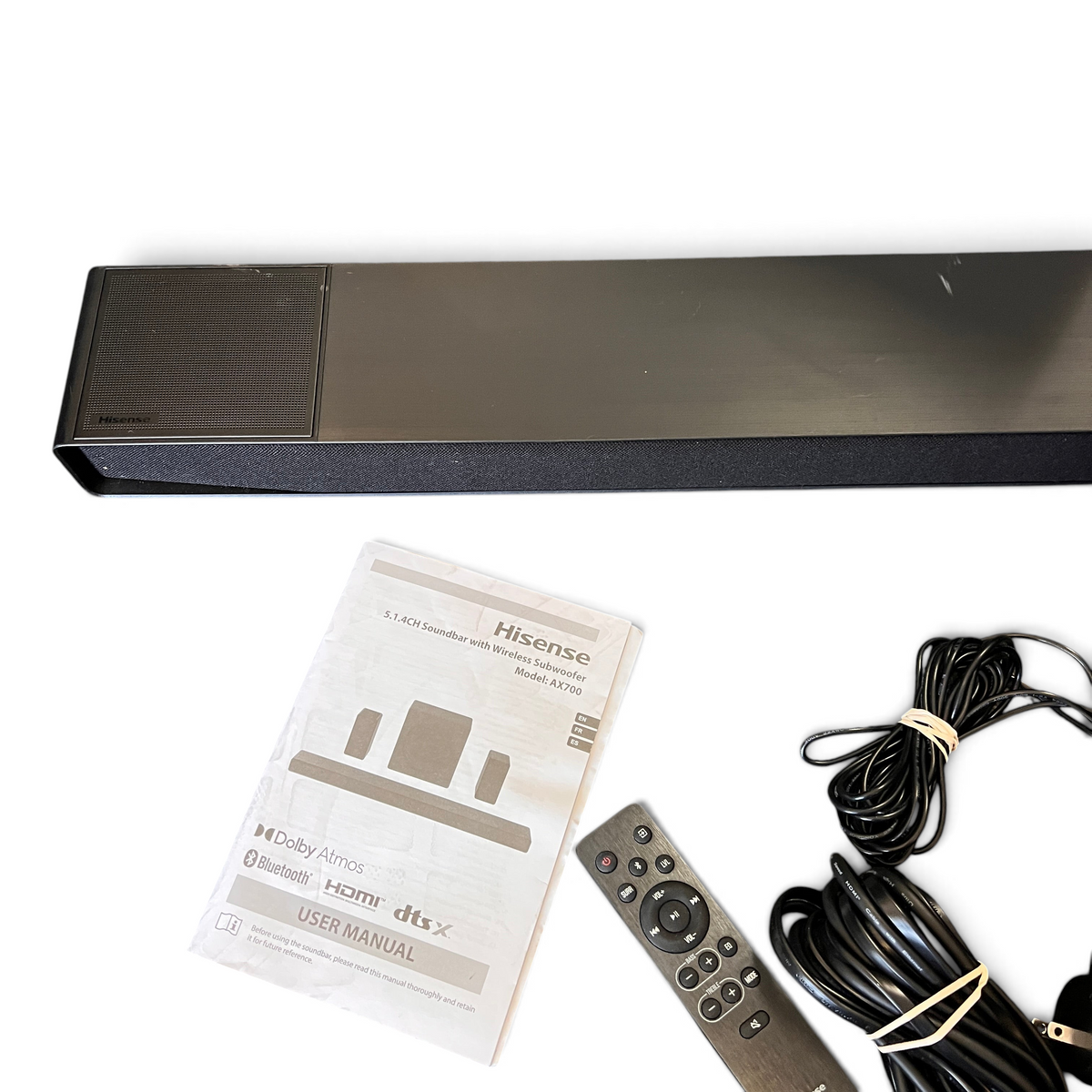 WT Outlets Hisense AX700 5.1.4 channel soundbar system with remote, manual, and cables on a grey carpet background.